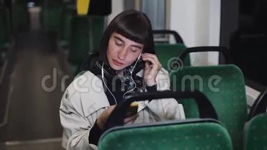 年轻时尚的女人戴着耳机，在公共交通工具上听手机音乐。 城市灯光